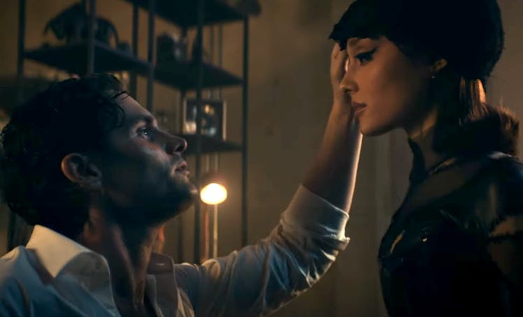 A man with tousled hair gazes up at a woman in a beret, who gently touches his face, in a dimly lit,...