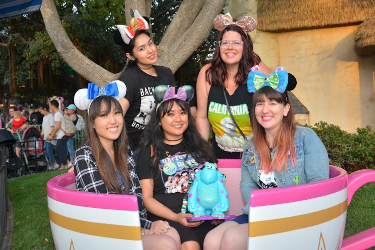 A group of friends wearing Minnie ears are sitting in a teacup spending a day at Disneyland.