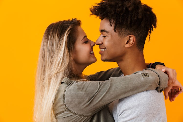 Portrait of a young multhiethnic couple isolated over yellow background, hugging