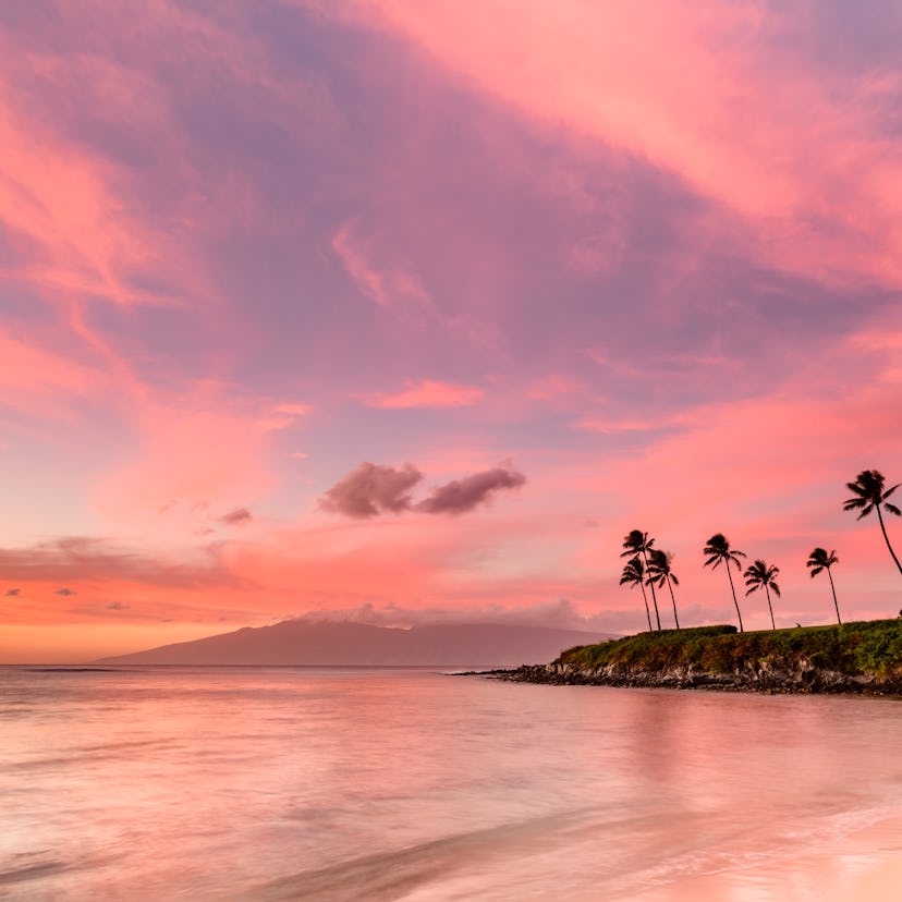 A serene beach at sunset with gentle waves lapping the shore, vibrant pink and orange skies, and a l...