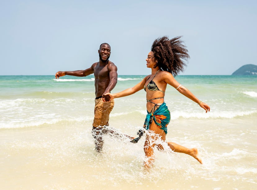 Happy couple enjoying a sunny day at the beach, splashing through the waves. Capturing the essence o...